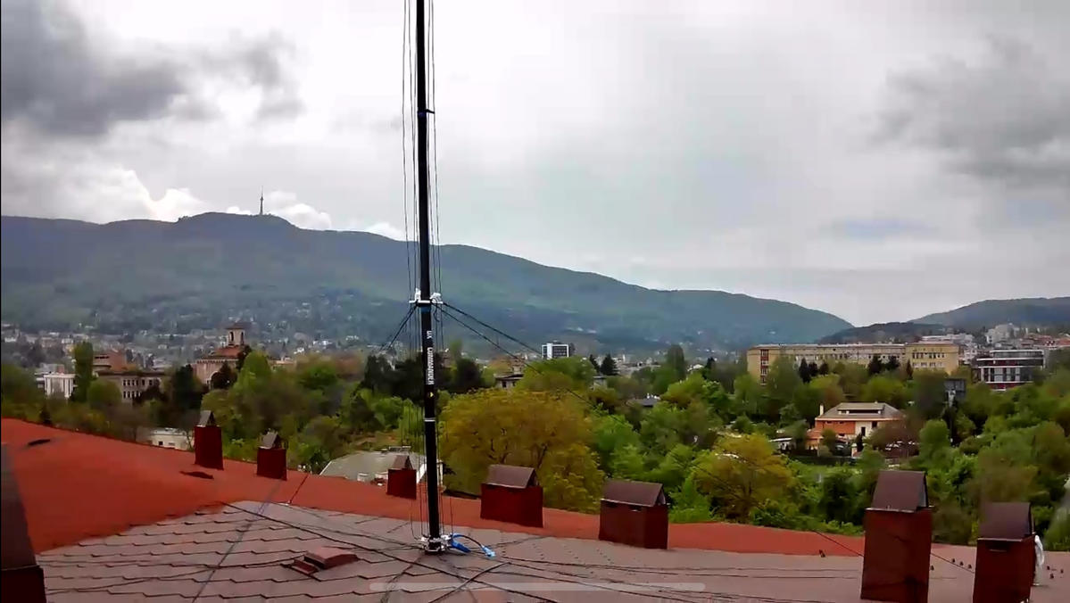 DX Commander vertical antenna on rooftop with city and mountain view